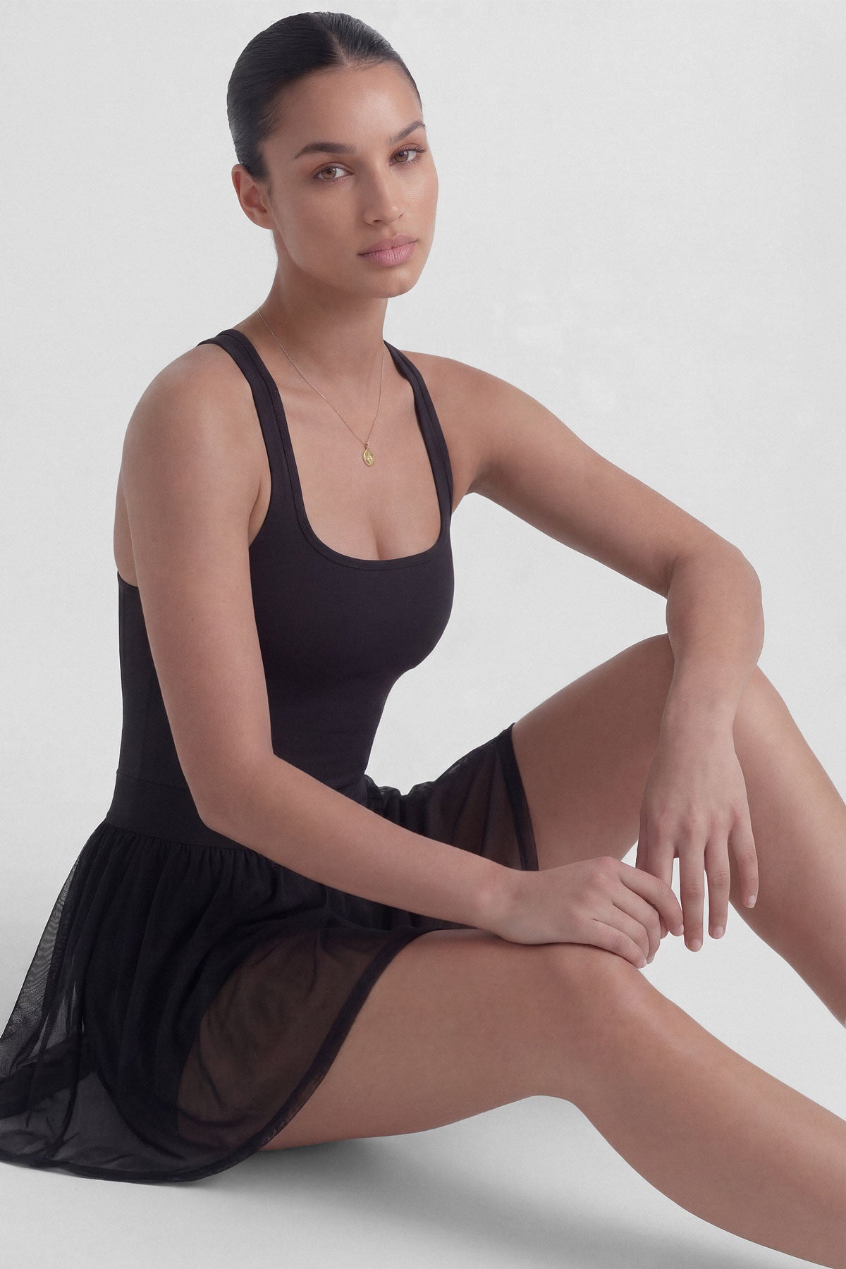Black tennis dress with square neckline, racerback, sculpting bodice, and sheer mesh skirt with built-in shorts