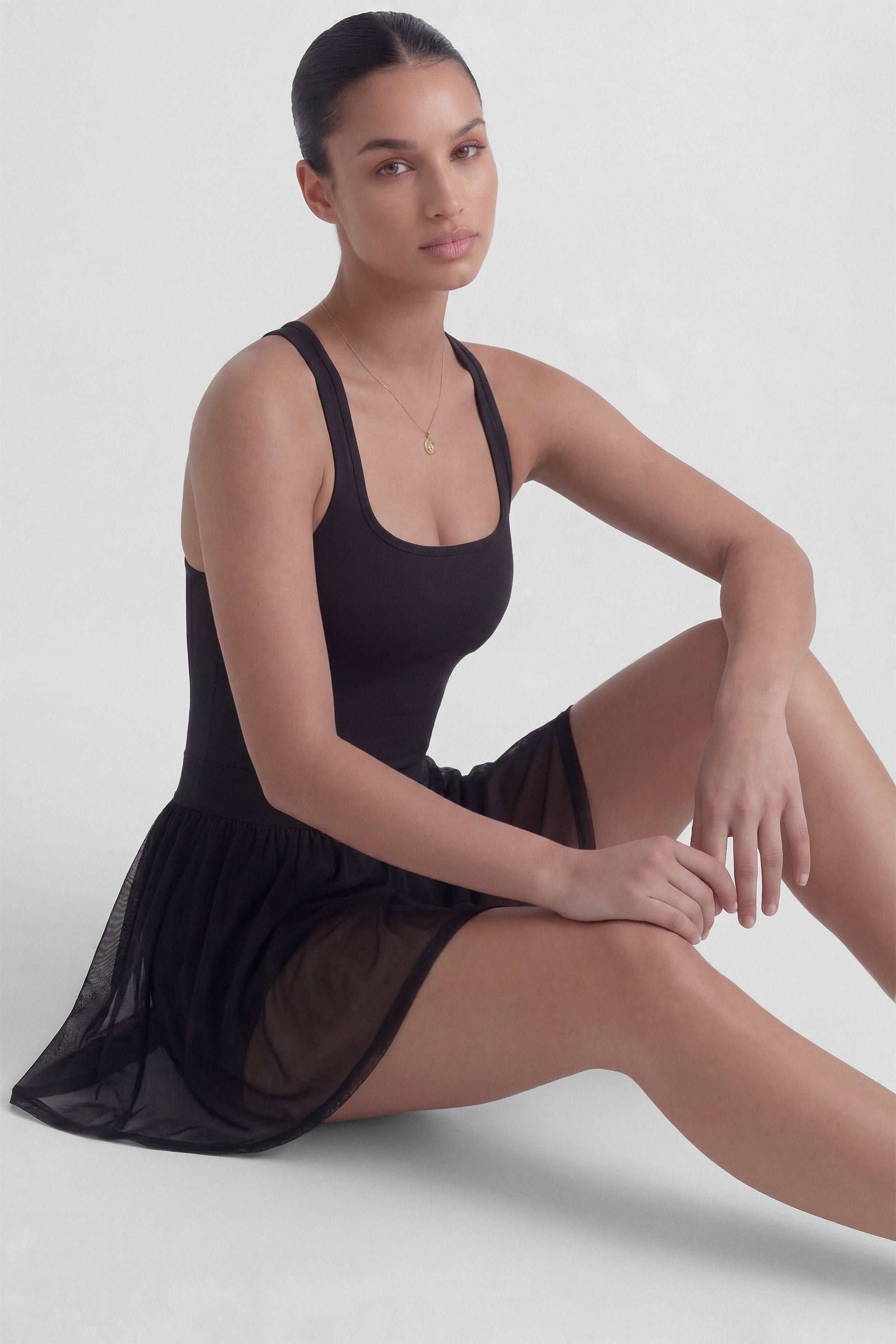 Black tennis dress with square neckline, racerback, sculpting bodice, and sheer mesh skirt with built-in shorts from Common Player