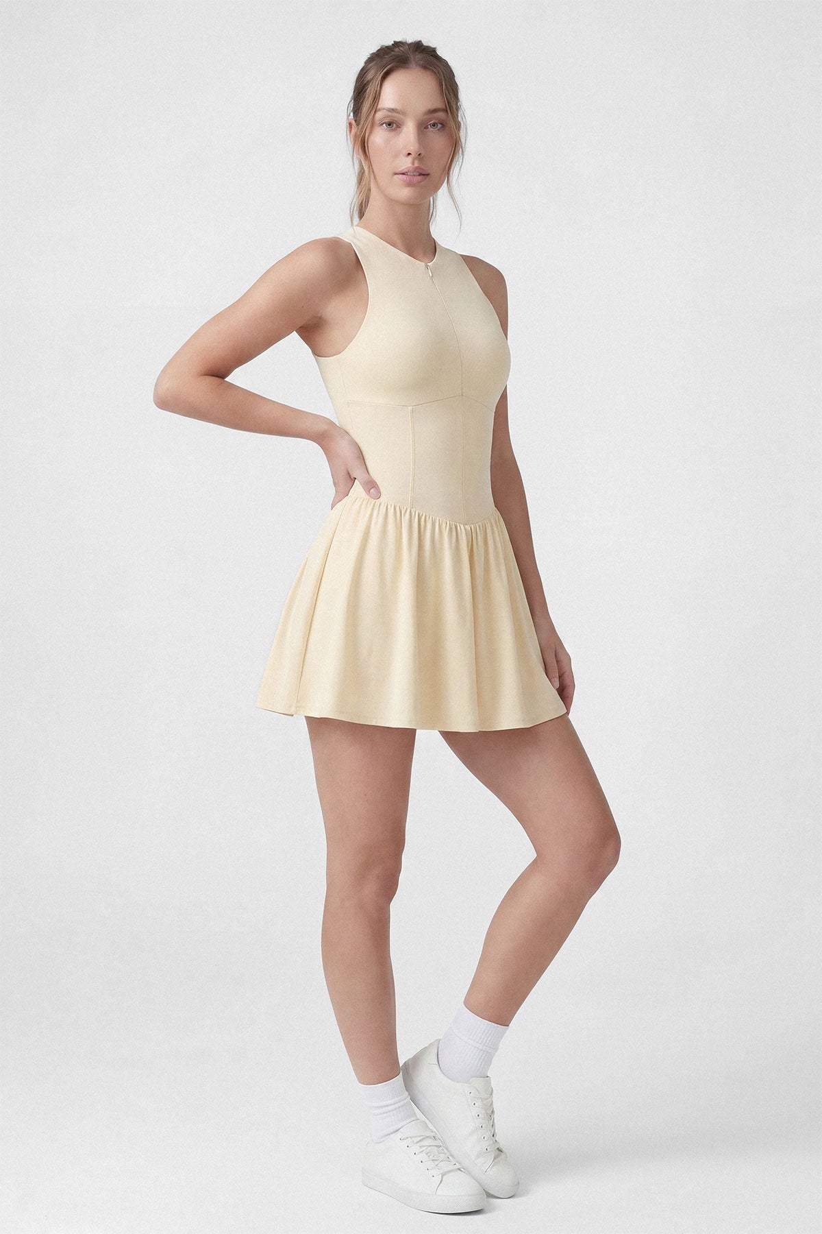 A butter yellow sleeveless tennis dress with a zipper closure, built-in shorts and a pocket