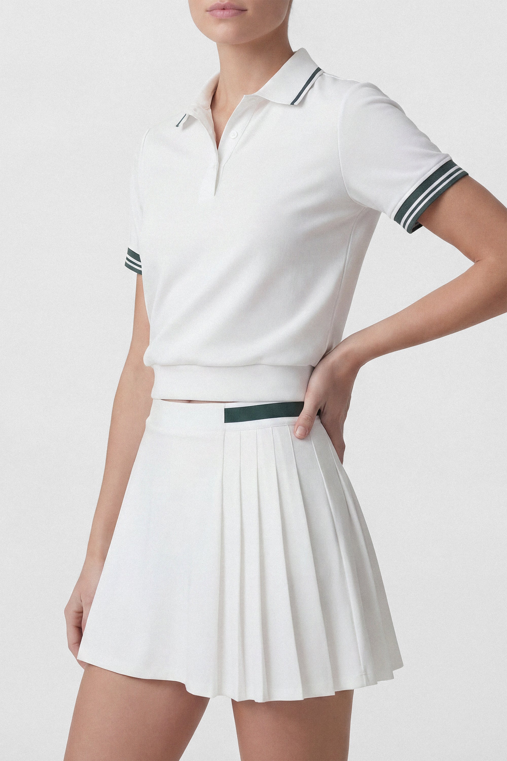 Model wearing a white pleated golf skirt with built in shorts and green stripe and a white golf polo top