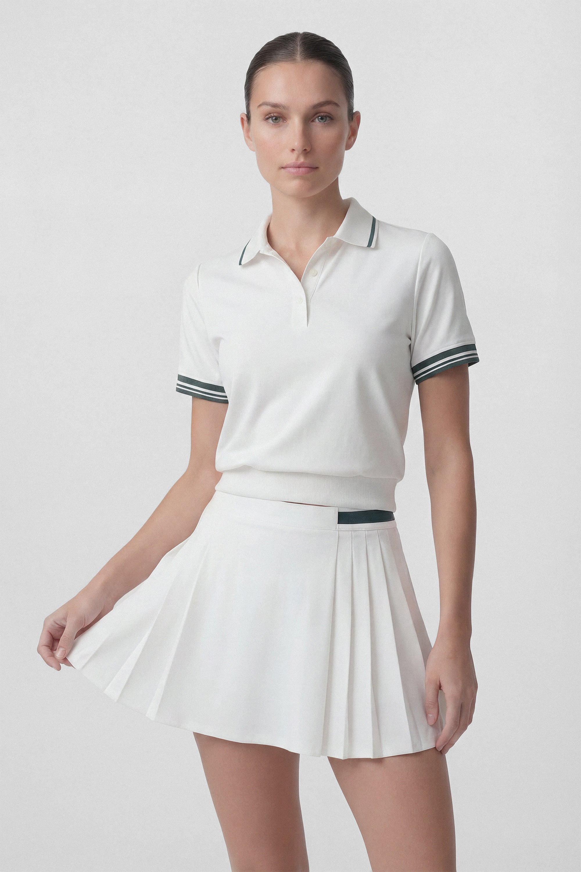 Model wearing a white pleated golf skirt with built in shorts and green stripe and a white golf polo top